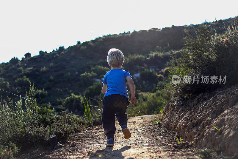 A young boy is running on a single track in the mountains